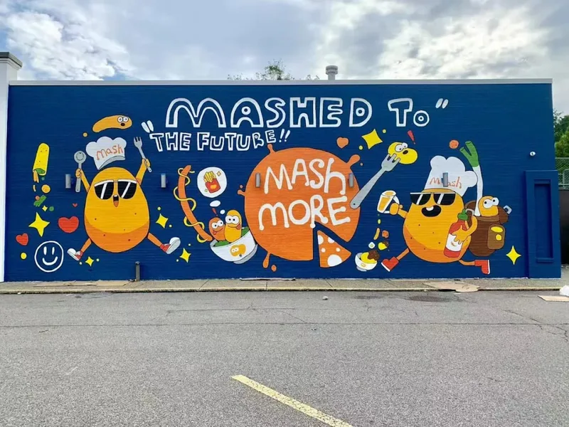 The MashMore mural: two cartoon potatoes in sunglasses under the words Mashed to the Future, on a blue wall